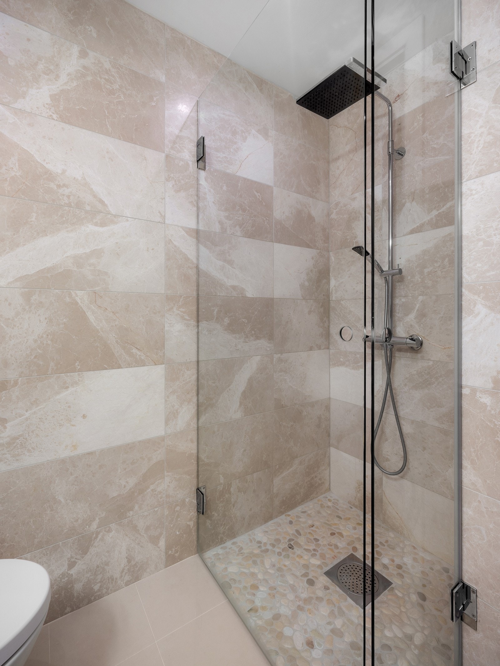 Innredet med vegghengt servant med glattfinerte fronter, helstøpt servantbenk og speil med belysning, dusjhjørne med dusjdører i herdet glass, waterfall-dusjhode og vegghengt armatur, samt vegghengt toalett. Galleribilde