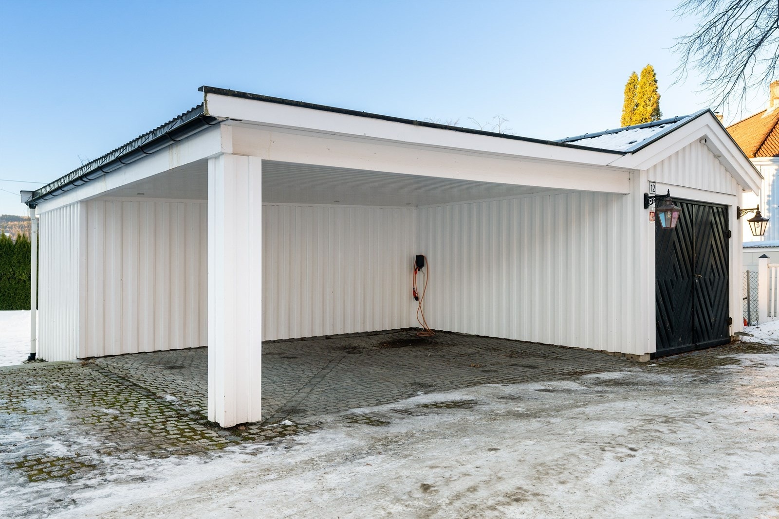 Romslig carport med rene linjer og integrert bod, en arkitektonisk og funksjonell løsning som harmonerer med eiendommens uttrykk. Galleribilde