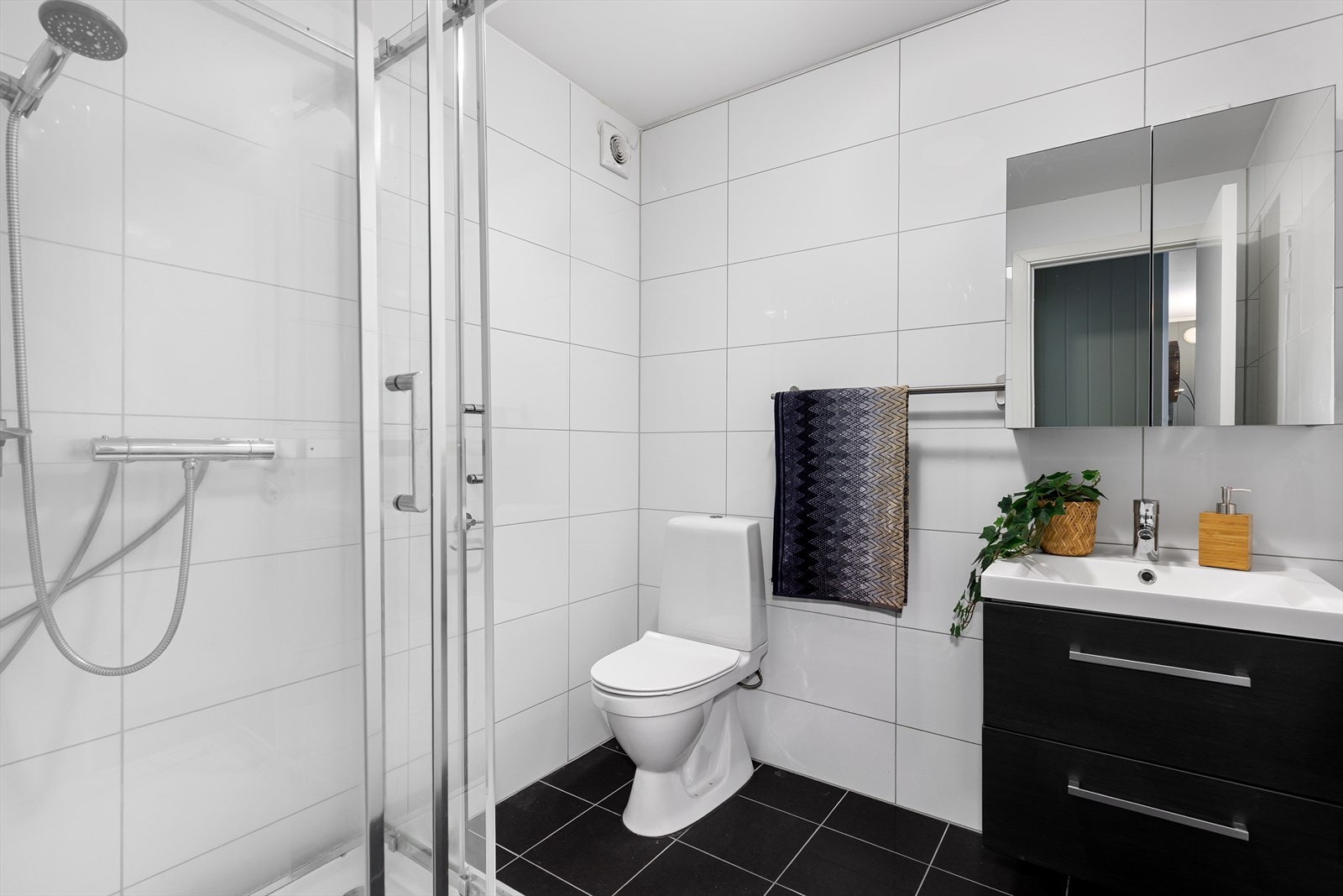 Lekkert flislagt bad med gulvvarme, dusjkabinett og vegghengt servant med skuffer for moderne og praktisk løsning. Galleribilde