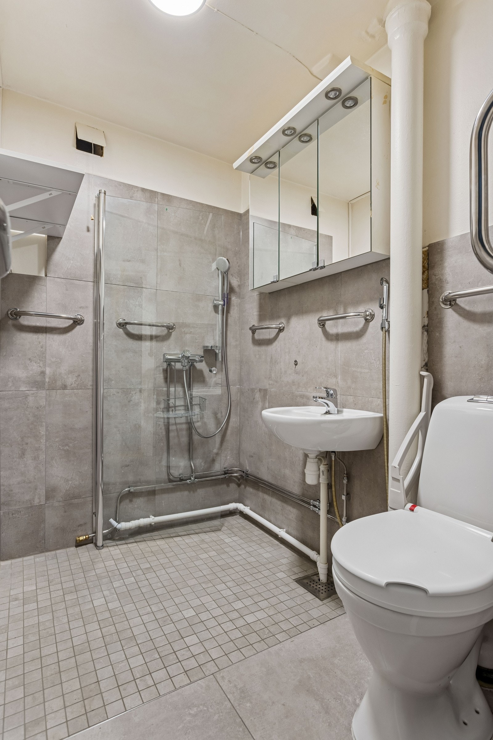 Flislagt baderom med dusj med inn/- utadslående dusjvegger, servant, overskap med speil, toalett og opplegg for vaskemaskin. Galleribilde