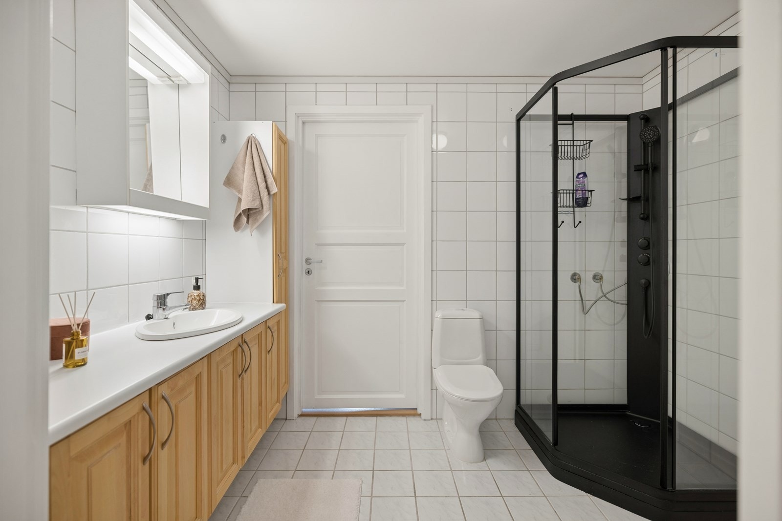 Lyst og funksjonelt bad med toalett, dusjkabinett og gjennomført flisvalg Galleribilde