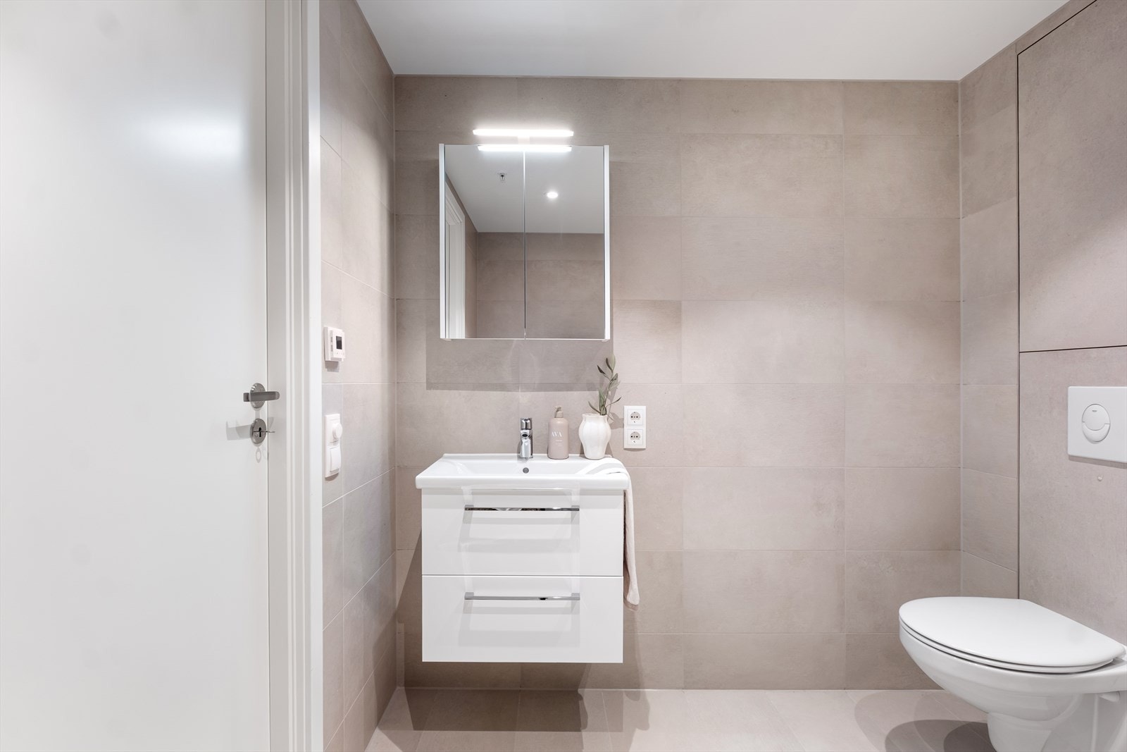 Vegghengt toalett og speil med belysning gir praktiske løsninger i rommet. Galleribilde