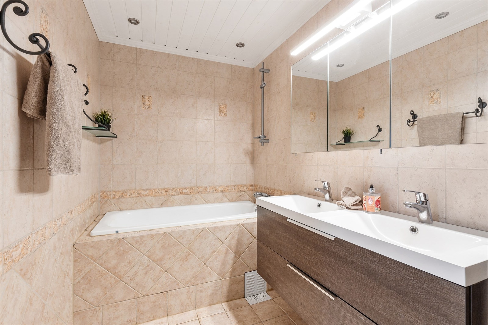 Badet er flislagt på gulv og vegger med elektrisk gulvvarme. Badet er innredet med badekar og en dobbel servant nedfelt i innredningen. Galleribilde