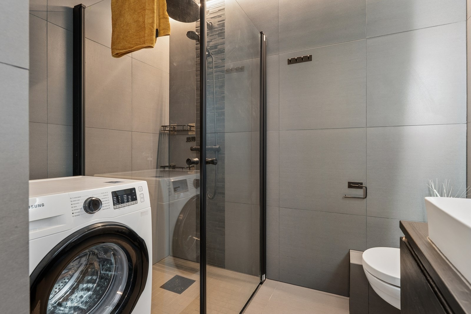 Badet er innredet med vegghengt toalett, dusjhjørne med glassvegger, innredning med servant og speil, samt opplegg for vaskemaskin. Galleribilde