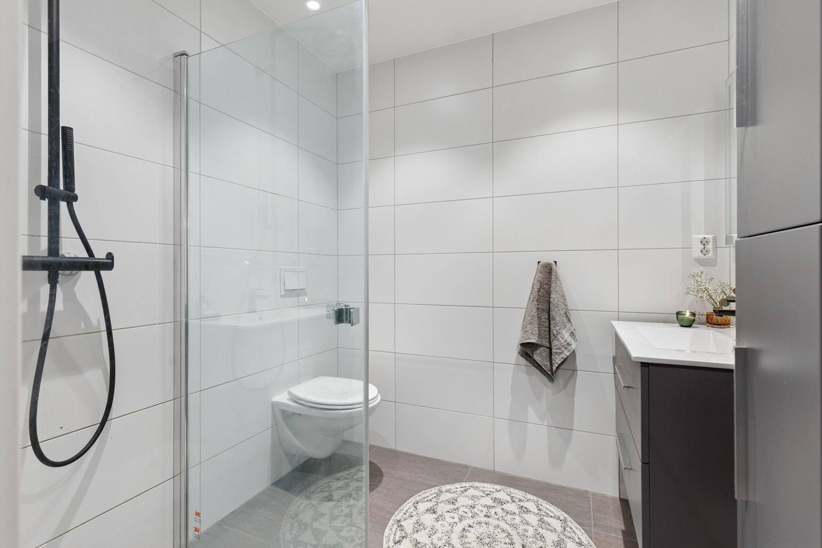 Flislagt og moderne bad med en praktisk planløsning. Badet er innredet med dusjnisje med glassvegg, vegghengt toalett og baderomsinnredning med servant og oppbevaringsplass. Galleribilde