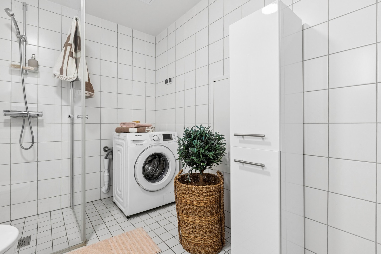 Badet har opplegg for vaskemaskin, dusjhjørne med glassdører, vegghengt toalett og hvit baderomsinnredning med god oppbevaringsplass. Galleribilde