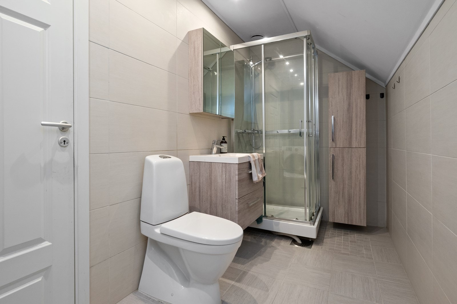 Nyere baderomsinnredning med servant med rom for oppbevaring i skuffeseksjon, speil, toalett og dusjkabinett. Rommet har opplegg for vaskemaskin. Galleribilde