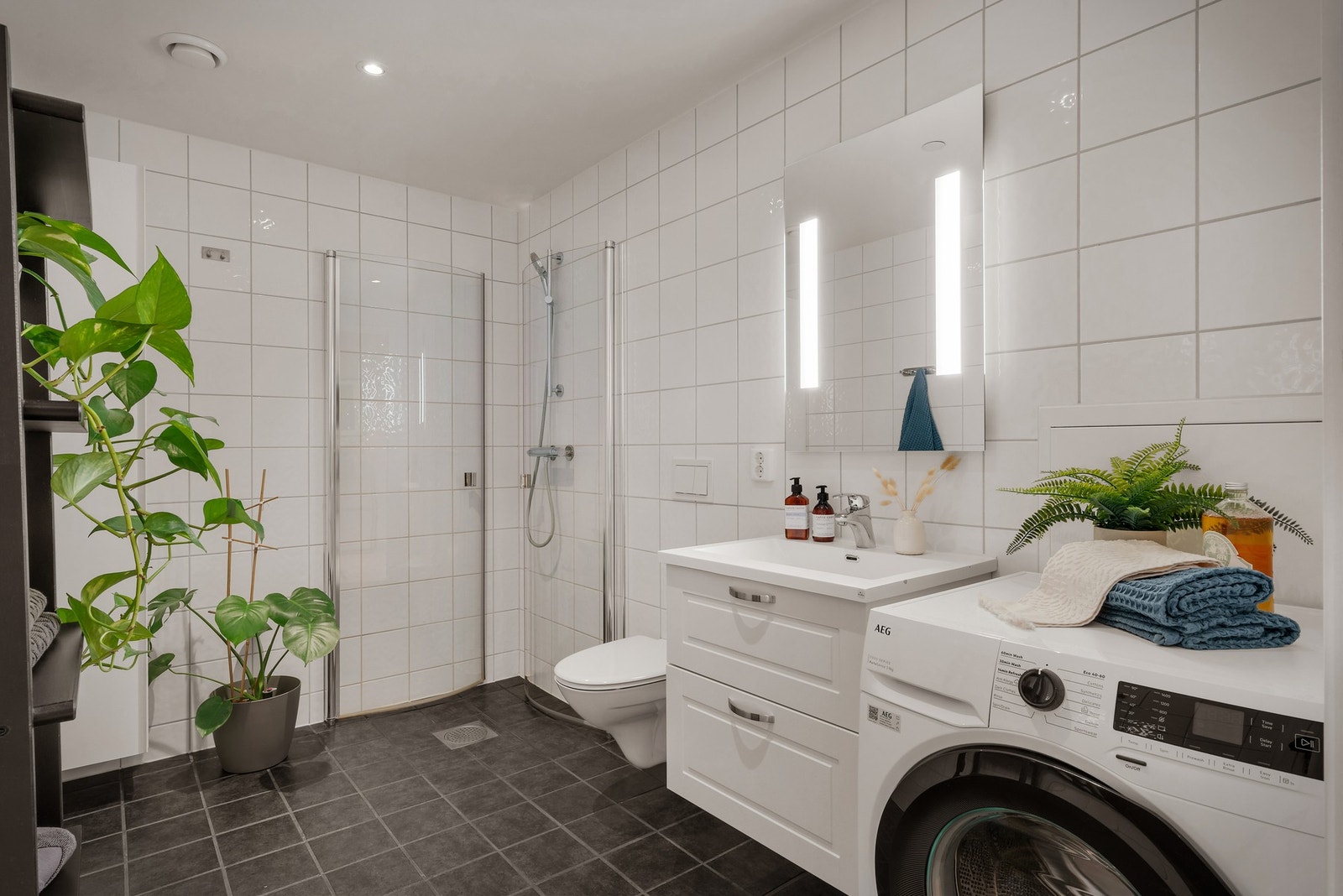 - Badet er innredet med flislagte gulv og vegger, vegghengt toalett, servant med skuffer under, dusjdører i klart glass samt opplegg for vaskemaskin - Galleribilde