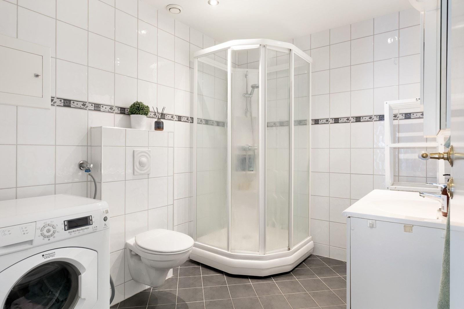 Badet har flisar på golv og veggar. Her har du dusjkabinett, veggmontert toalett, servantskap med heilstøypt servant og opplegg for vaskemaskin. Galleribilde