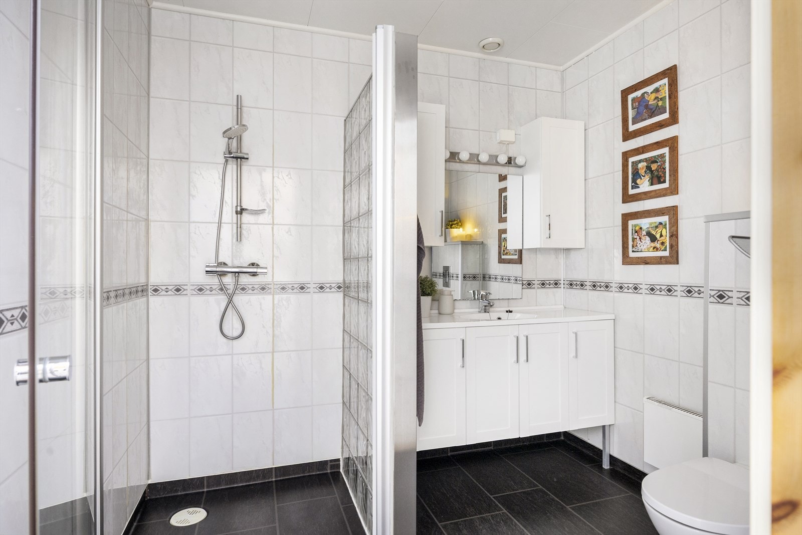 Badet i første etasje tilbyr fin innredning med servant nedfelt i benkeskap, vegghengt toalett, dusjhjørne med glassbyggerstein, speil og veggskap Galleribilde