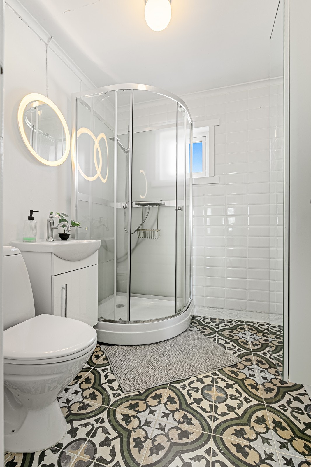 Badet har flislagt gulv med varmekabler og flis/våtromstapet på vegger. Badet inneholder toalett, dusjkabinett og servant med innredning. Galleribilde