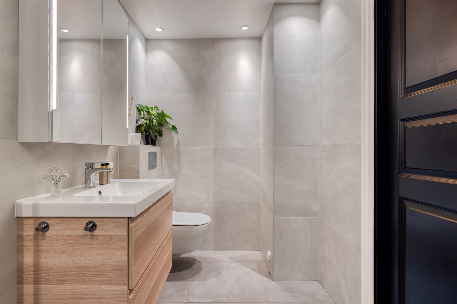 Badet er innredet med skap og ovenpåliggende servant, speilskap med belysning, vegghengt toalett. Galleribilde