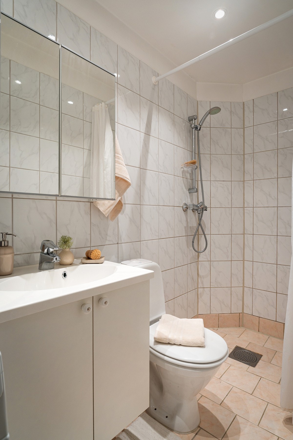 Badet er flislagt og har en praktisk og funksjonell utforming. Innredningen består av servantskap med nedfelt servant og speilskap over, toalett samt dusjhjørne avskjermet med dusjvegger. Galleribilde