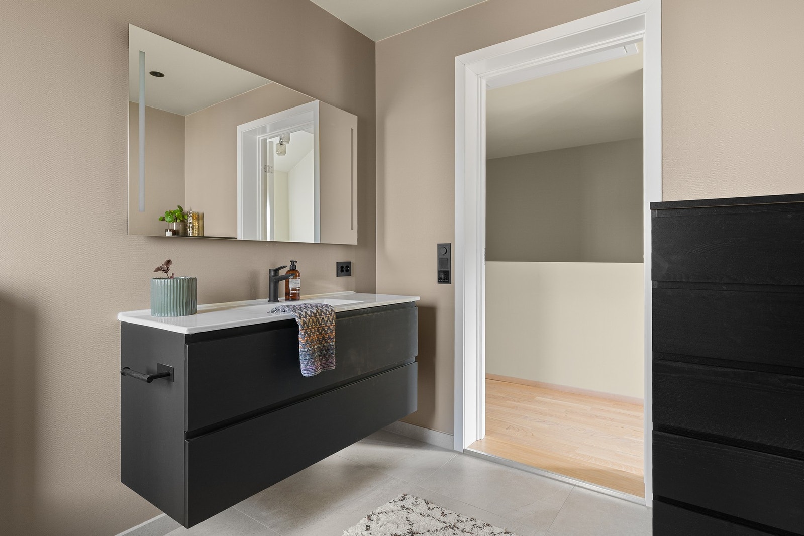 Badet er innredet med servant på skuffeseksjon og speil med belysning. Videre er rommet utstyrt med dusjdører, vegghengt toalett og opplegg til badekar. Galleribilde