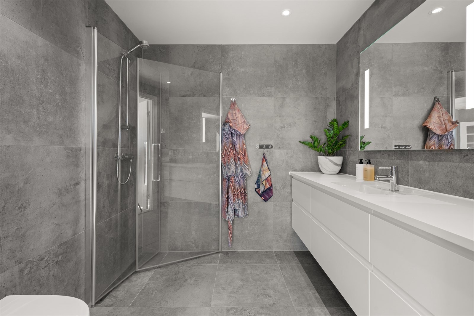 Delikat bad 2 i harmonisk stil med boligens øvrige bad, utstyrt med heldekkende servant på underskap, speil og integrert belysning. Galleribilde