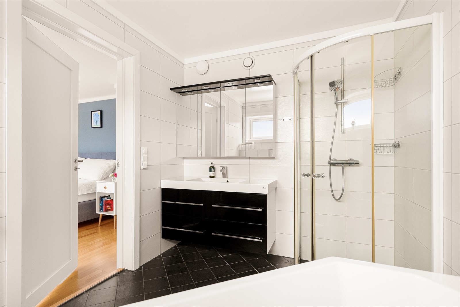 Lekkert flislagt bad med inngang fra hovedsoverommet - servant- og speilskap med god lagringsplass, samt praktisk dusjnisje. Galleribilde