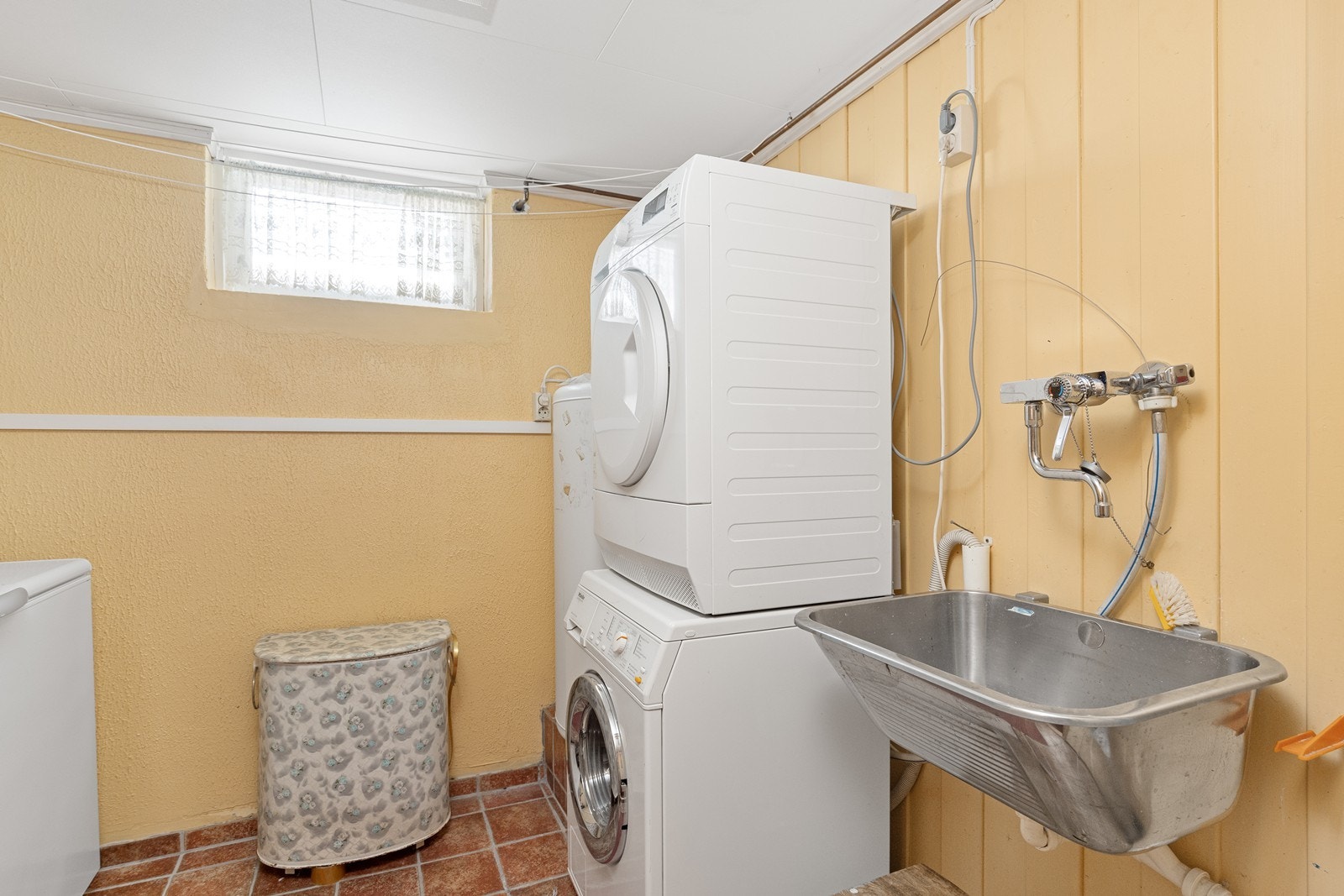 Praktisk vaskerom med flislagt gulv med gulvvarme, utslagsvask og opplegg for vaskemaskin. Galleribilde