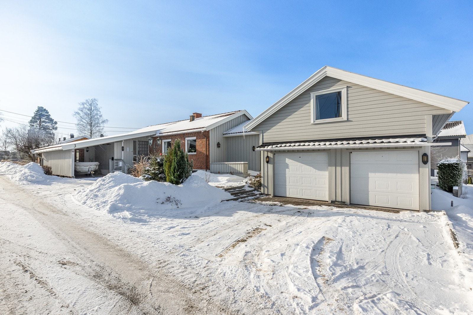 Enebolig med stor, frittliggende garasje med innredet hems, samt carport ved inngangspartiet. Galleribilde