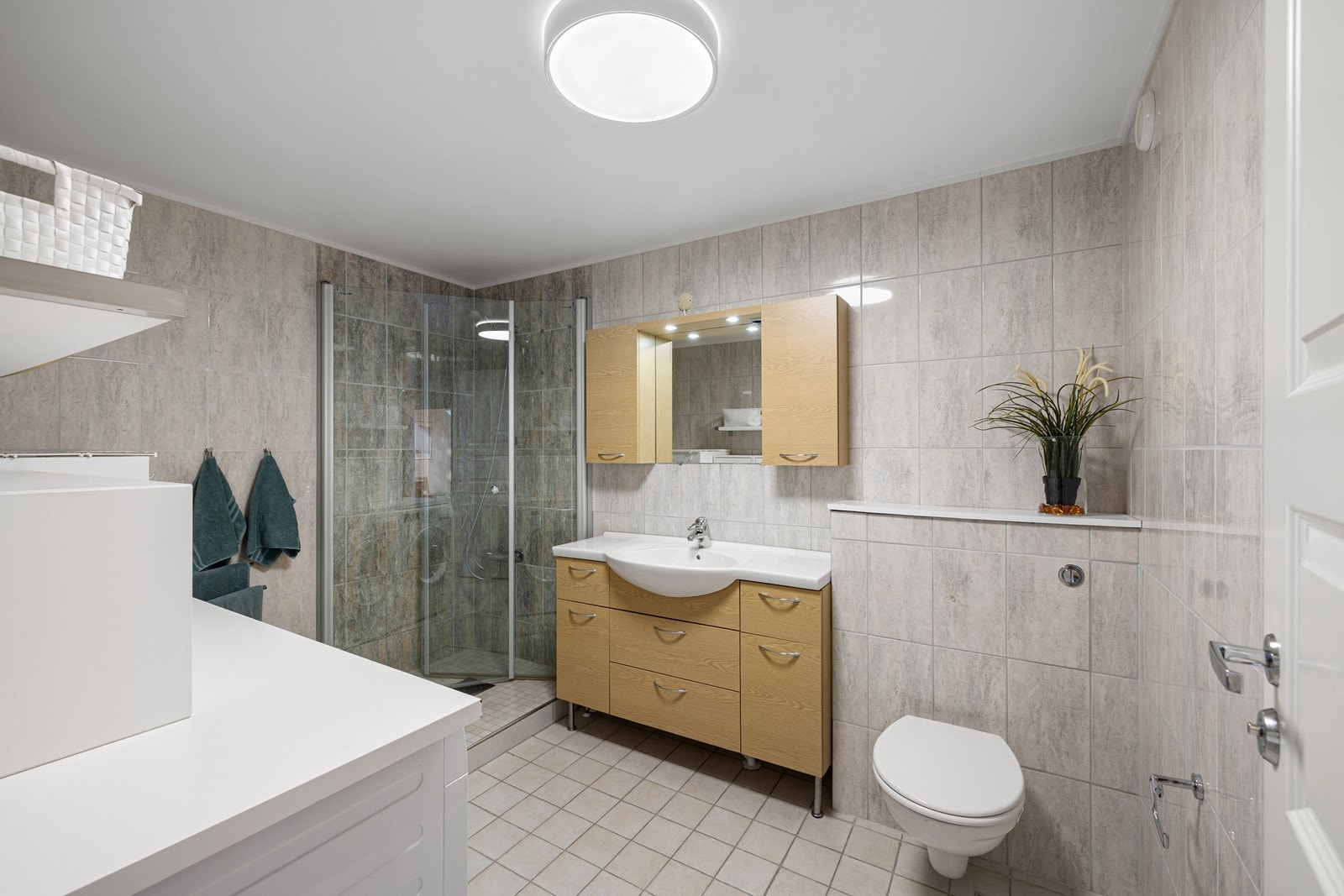 Boligen har et romslig bad med fliser på gulv og vegger. Innredningen består av et underskap/overskap, servant, speil og armatur med stikk og et dusjhjørne med glassdører. Galleribilde