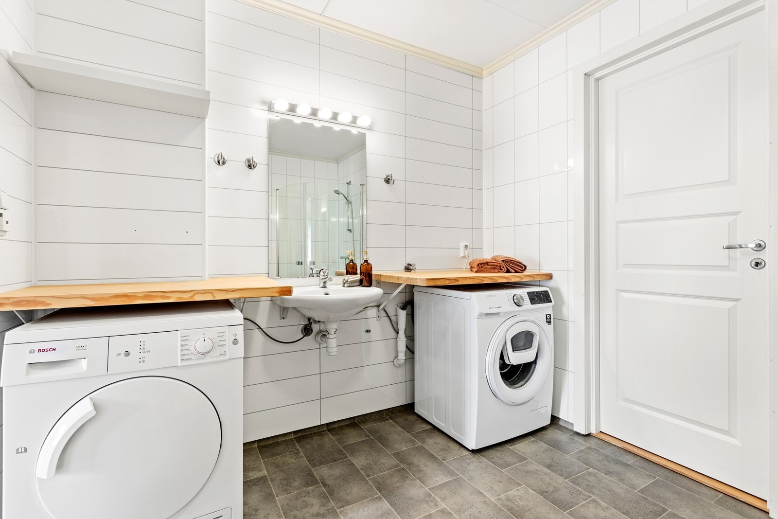 Badet inneheld alt ein trenger. Det er innreia med dusjhjørne med glasdører, klosett, enkel servant, spegel, og opplegg for både vaskemaskin og tørketrommel med arbeidsbenk. Frå badet er det tilkomst til bod der varmtvasstank er plassert. Galleribilde