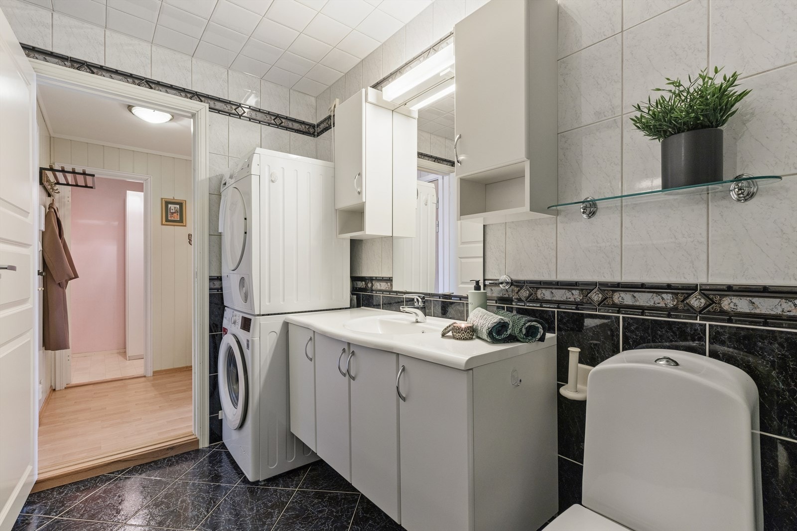 Badet er innredet med servant med underskap og ettgreps armatur, speil med sideskap og belysning, gulvstående toalett samt dusjkabinett. Det er opplegg for vaskemaskin. Galleribilde