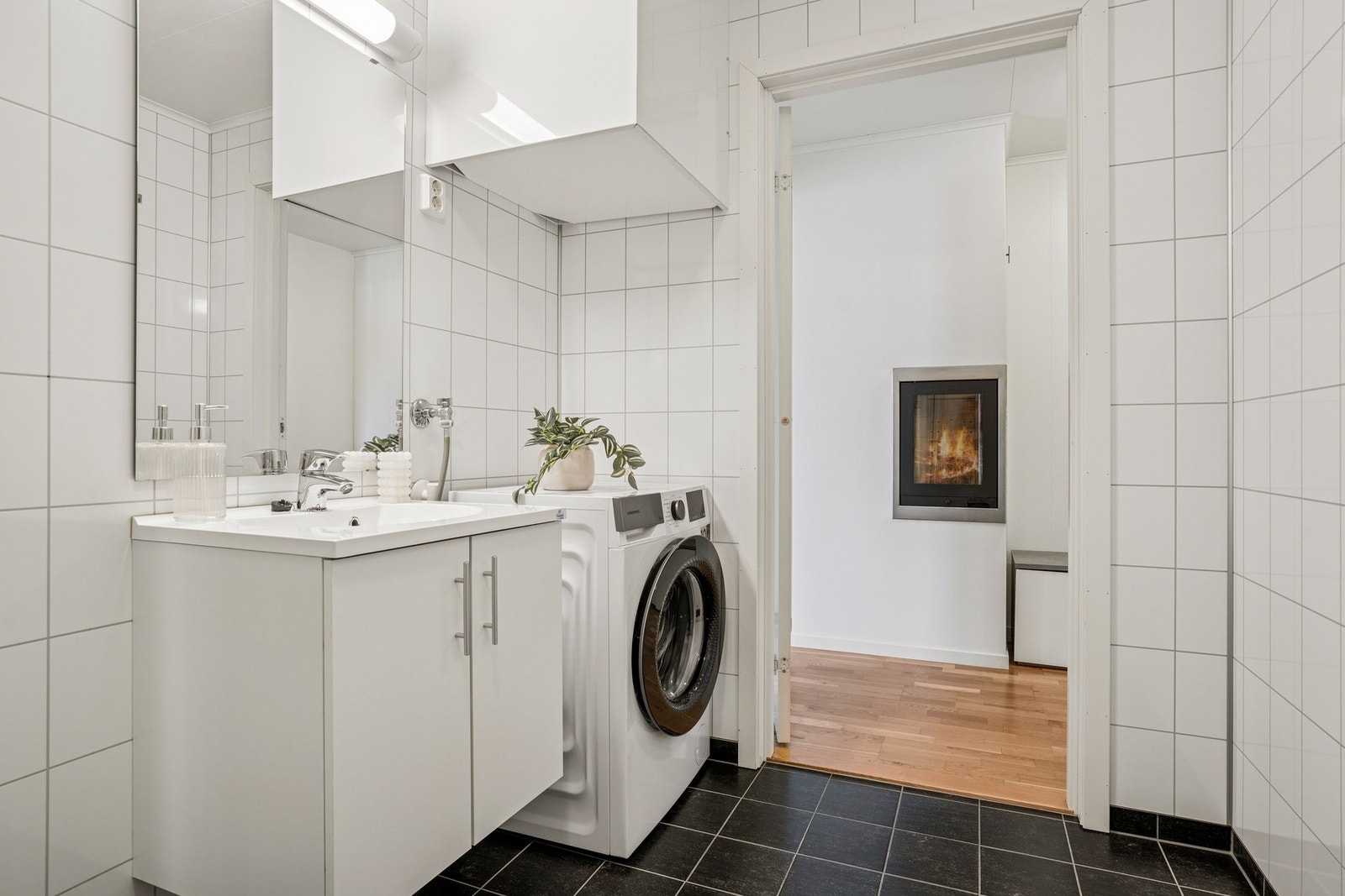 Badet er innredet med servant, speil med lys, toalett, opplegg for vaskemaskin og dusjkabinett. Galleribilde