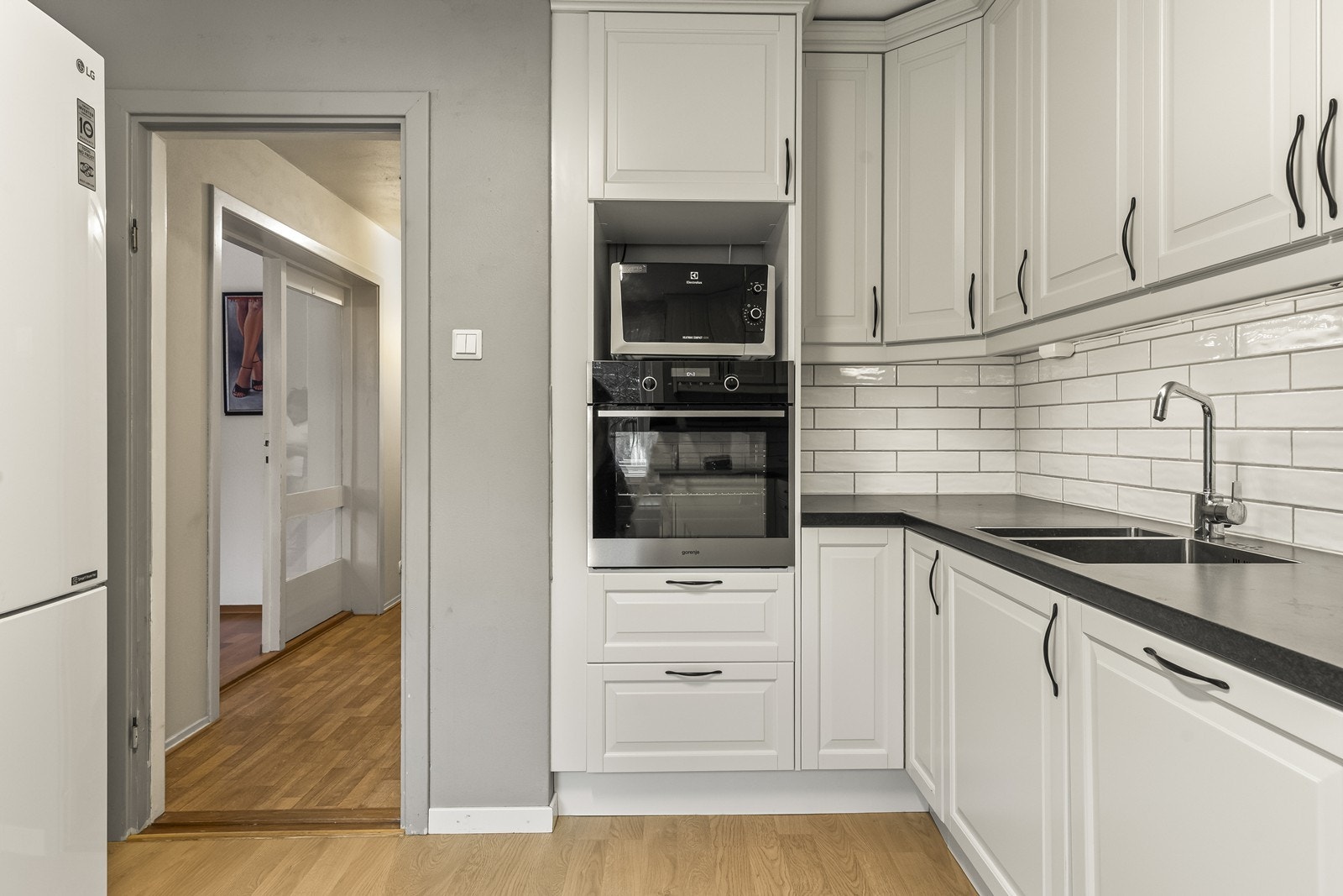 Den mørke laminatbenkeplaten gir en fin kontrast til innredningen, og det er flislagt mellom benkeplate og overskap for et praktisk og stilrent uttrykk. Kjøkkenet er utstyrt med integrerte hvitevarer. Galleribilde