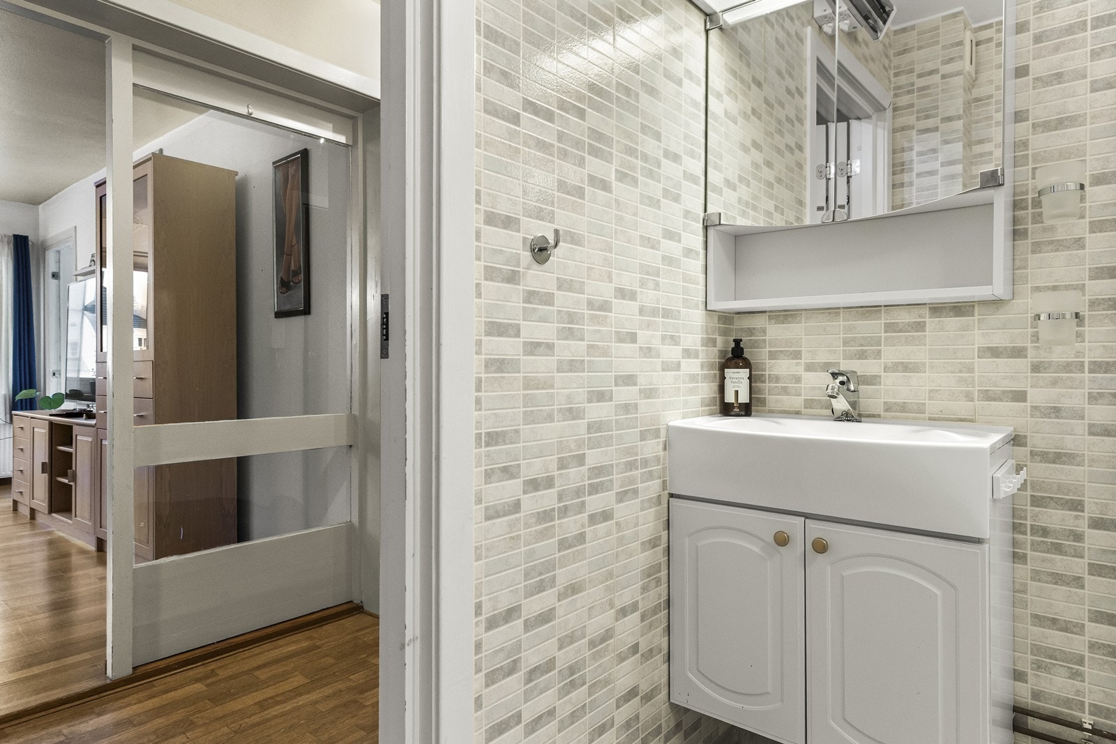 Bad har belegg på gulv og vinyltapet på vegger, samt en hvit baderomsinnredning med speil over. Galleribilde