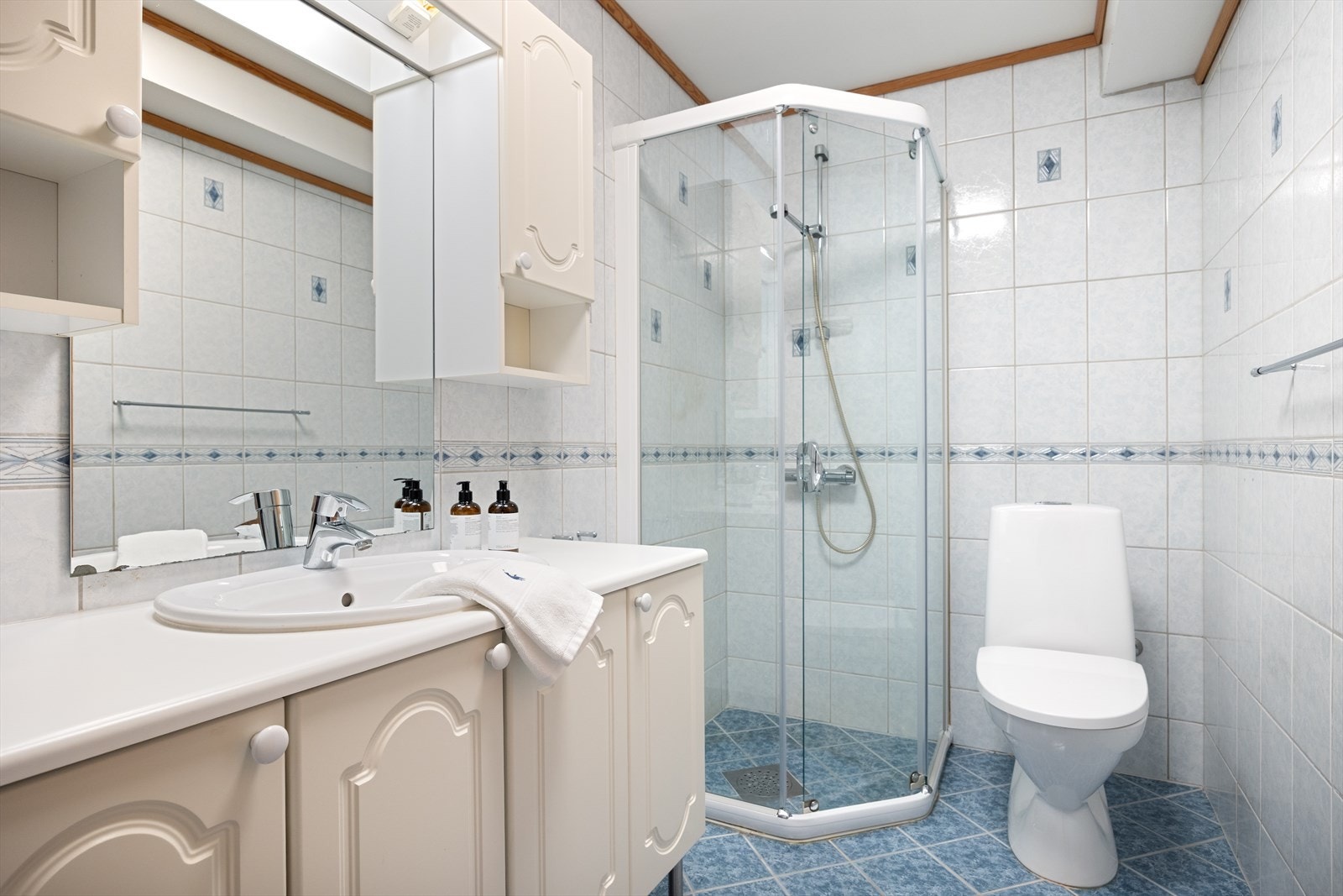 Flisbelagt bad i sokkeldel med dusjkabinett, toalett og servant. Galleribilde