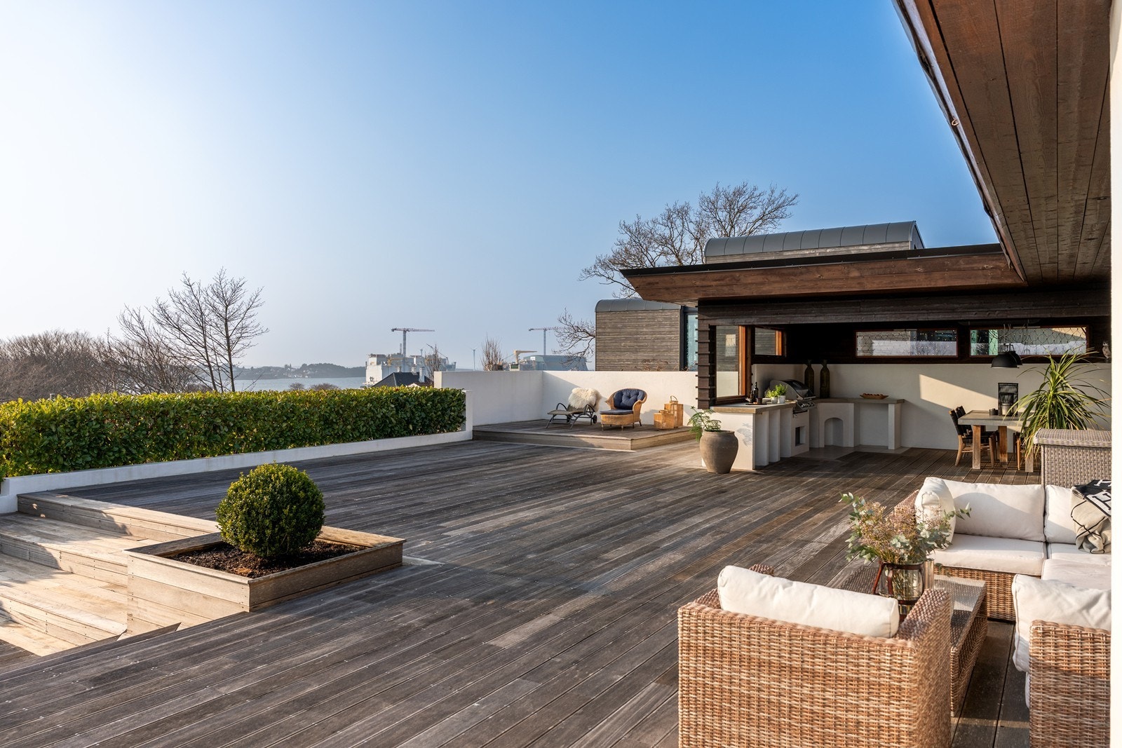 Eiendommens rause utearealer består av terrasse og hellebelagt platting i flere nivåer, i tillegg til overbygget del med utekjøkken på den ene siden av boligen, samt grønn plen på den andre siden. Galleribilde