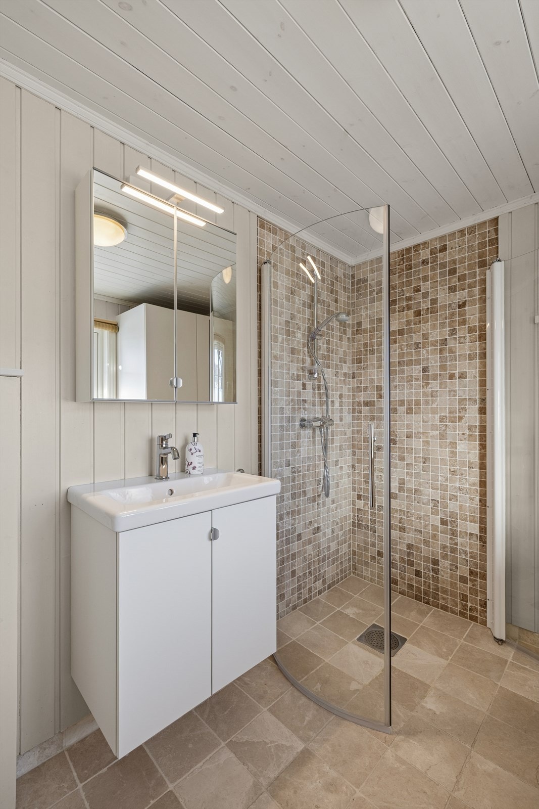 Badet er innredet med baderomsinnredning med servant, speilskap med belysning, dusjhjørne med innfellbare glassdører og vegghengt toalett. Galleribilde