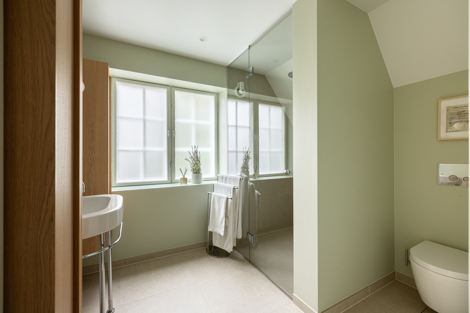 Pent baderom fra 2023 med vegghengt wc, servant med krom/stål ben med eik høyskap på begge sider og dusj i hjørne med glassdør/vegg. Galleribilde