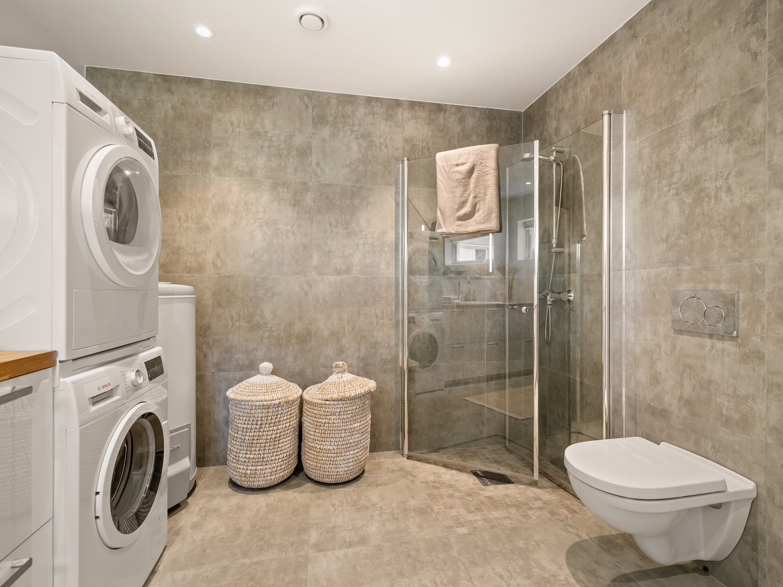 Bad/vaskerom er utstyrt med innredning med utslagsvask, opplegg for vaskemaskin, dusjhjørne med glassdører og vegghengt toalett. Galleribilde