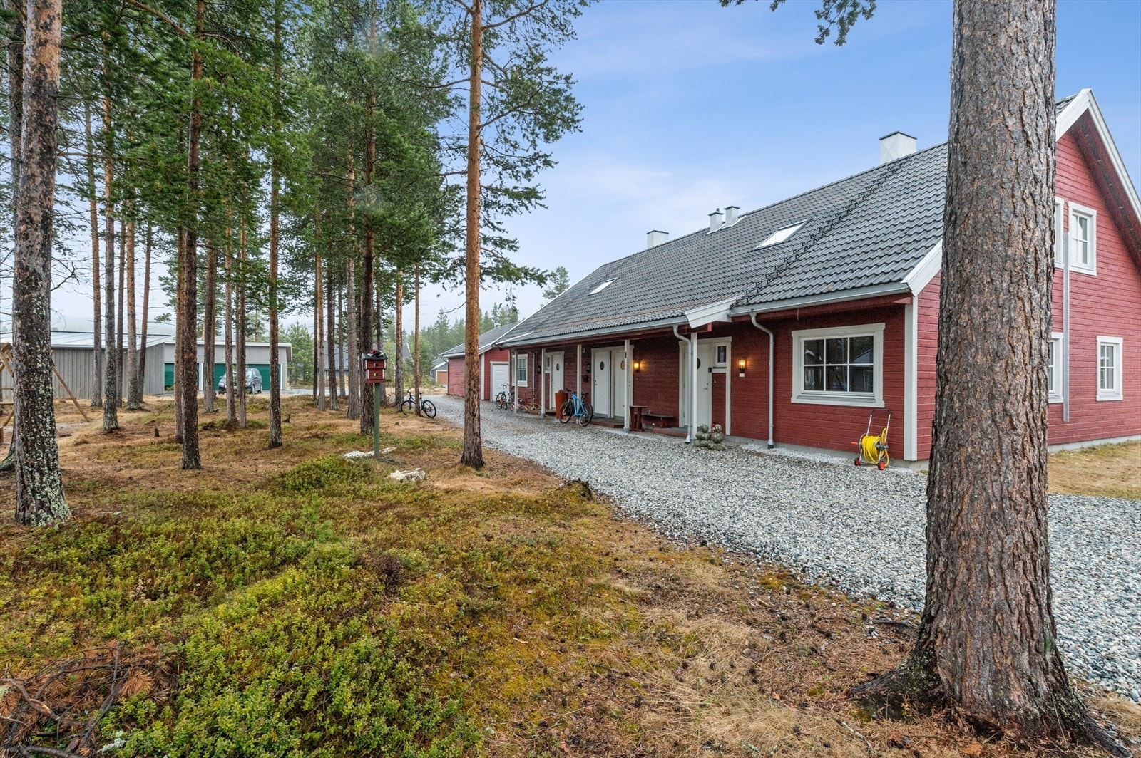 Eiendommen ligger på en flat tomt med gruset innkjørsel, omkranset av natur. Galleribilde
