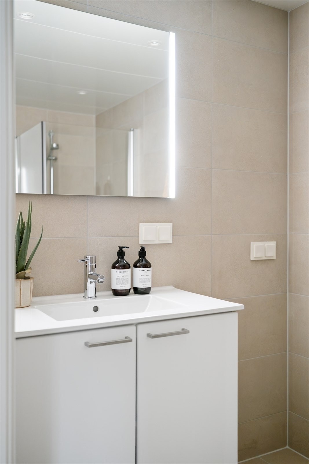Badet er innredet med vegghengt toalett, servant med innredning, speil med lys og dusjhjørne med svingbare glassdører. Galleribilde