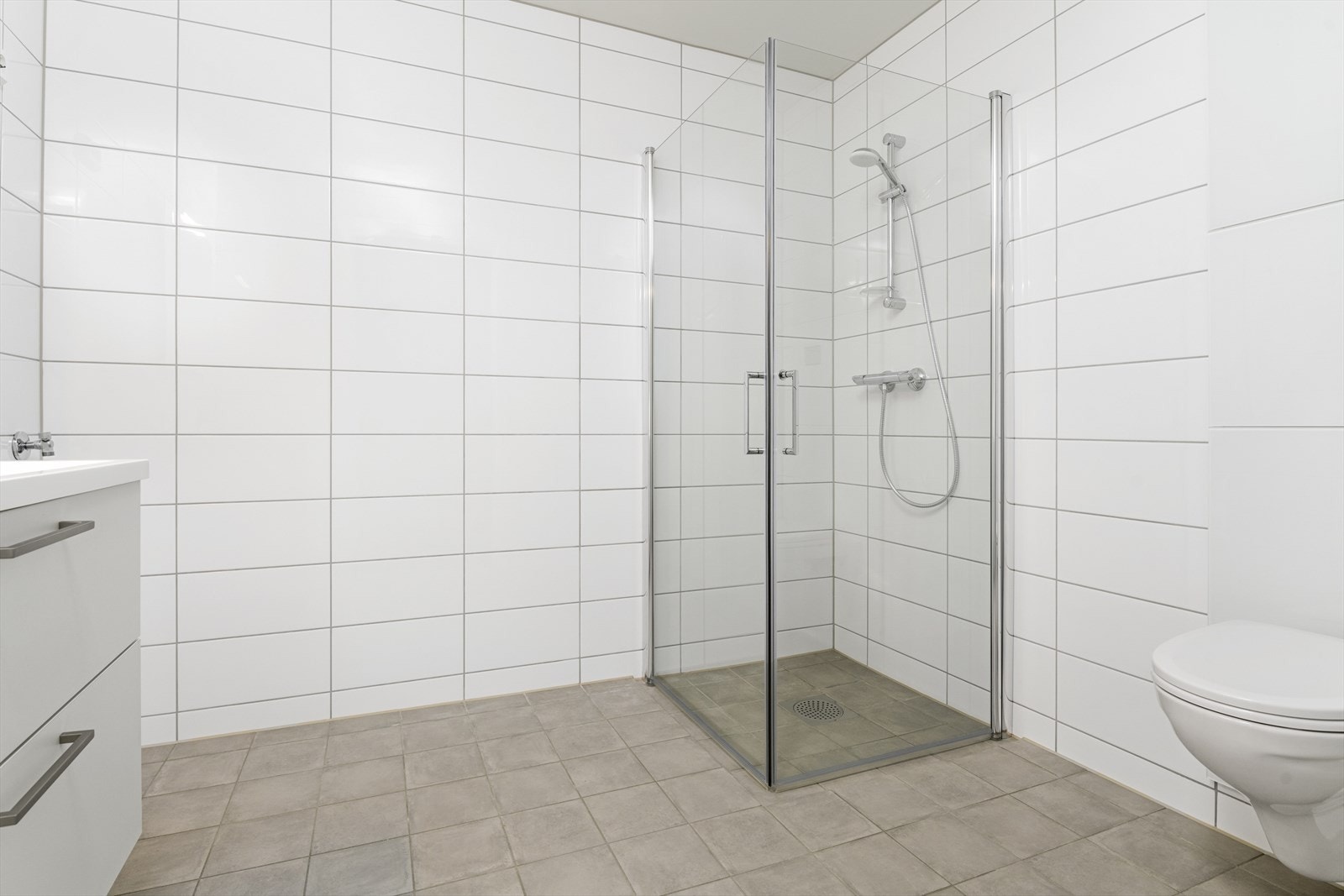 Romslig helfliset bad. Servant med nedfelt vask, vegghengt toalett og dusjhjørne. Det er vannbåren varme i gulv. Galleribilde