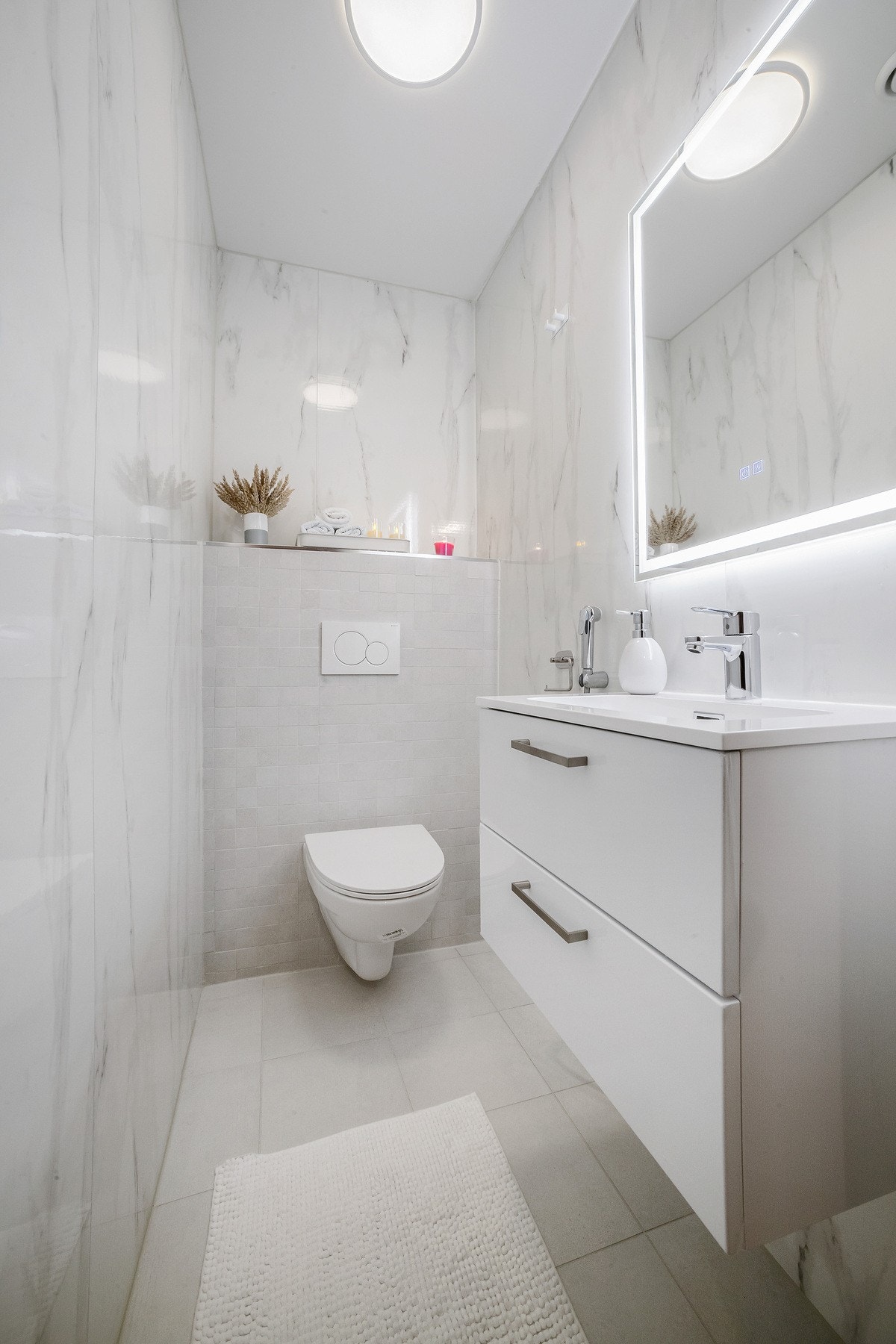 Ekstra vegghengt toalett, pent supplert av moderne flater, vask og lyssatt speil med servant under. Galleribilde