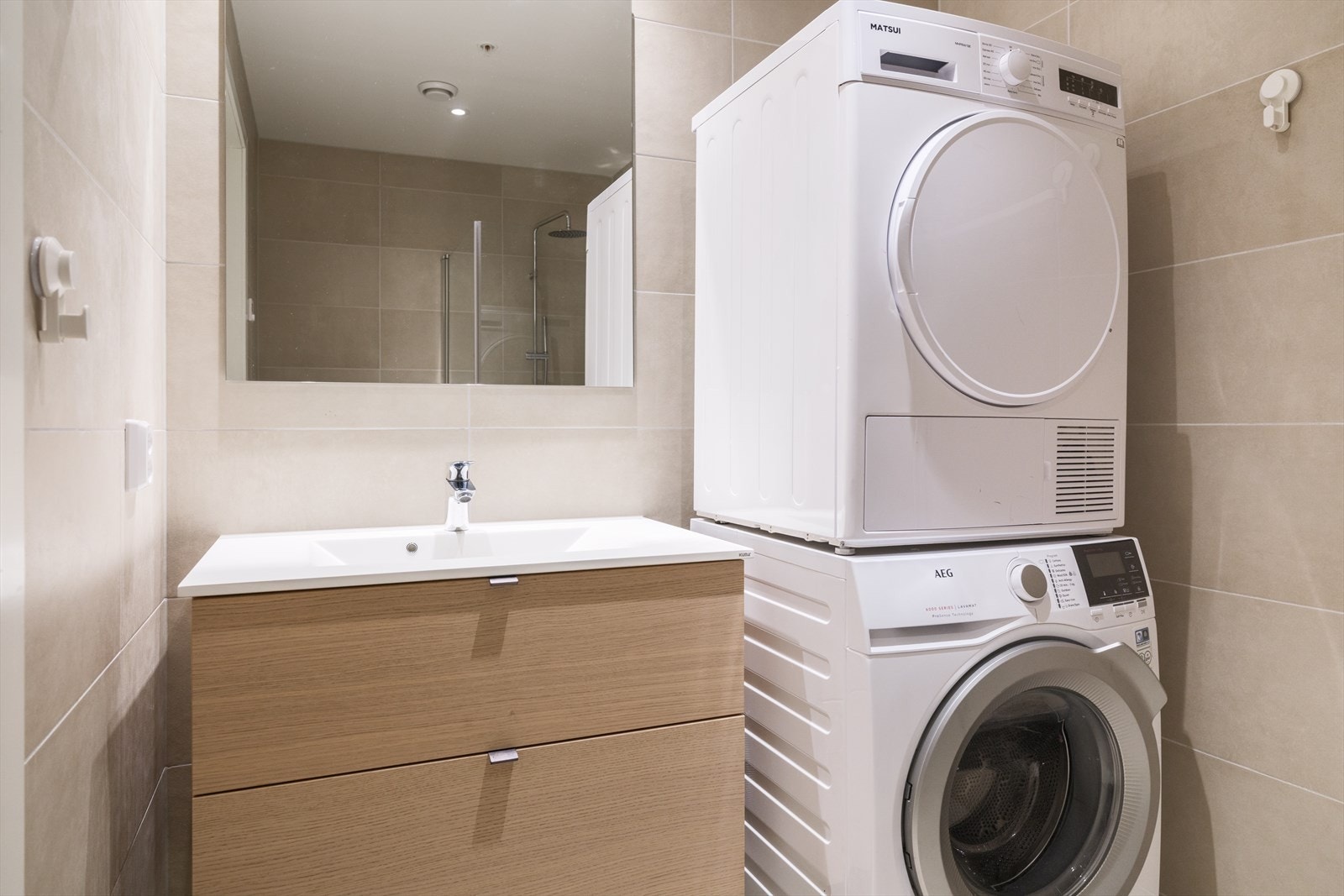 Stilren innredning med god oppbevaringsplass og praktisk løsning med opplegg for både vaskemaskin og tørketrommel Galleribilde