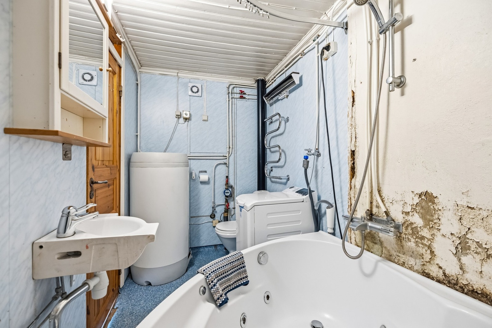 Fra en annen vinkel ser man badets installasjoner med varmtvannsbereder, vaskemaskin og sanitærutstyr. Galleribilde