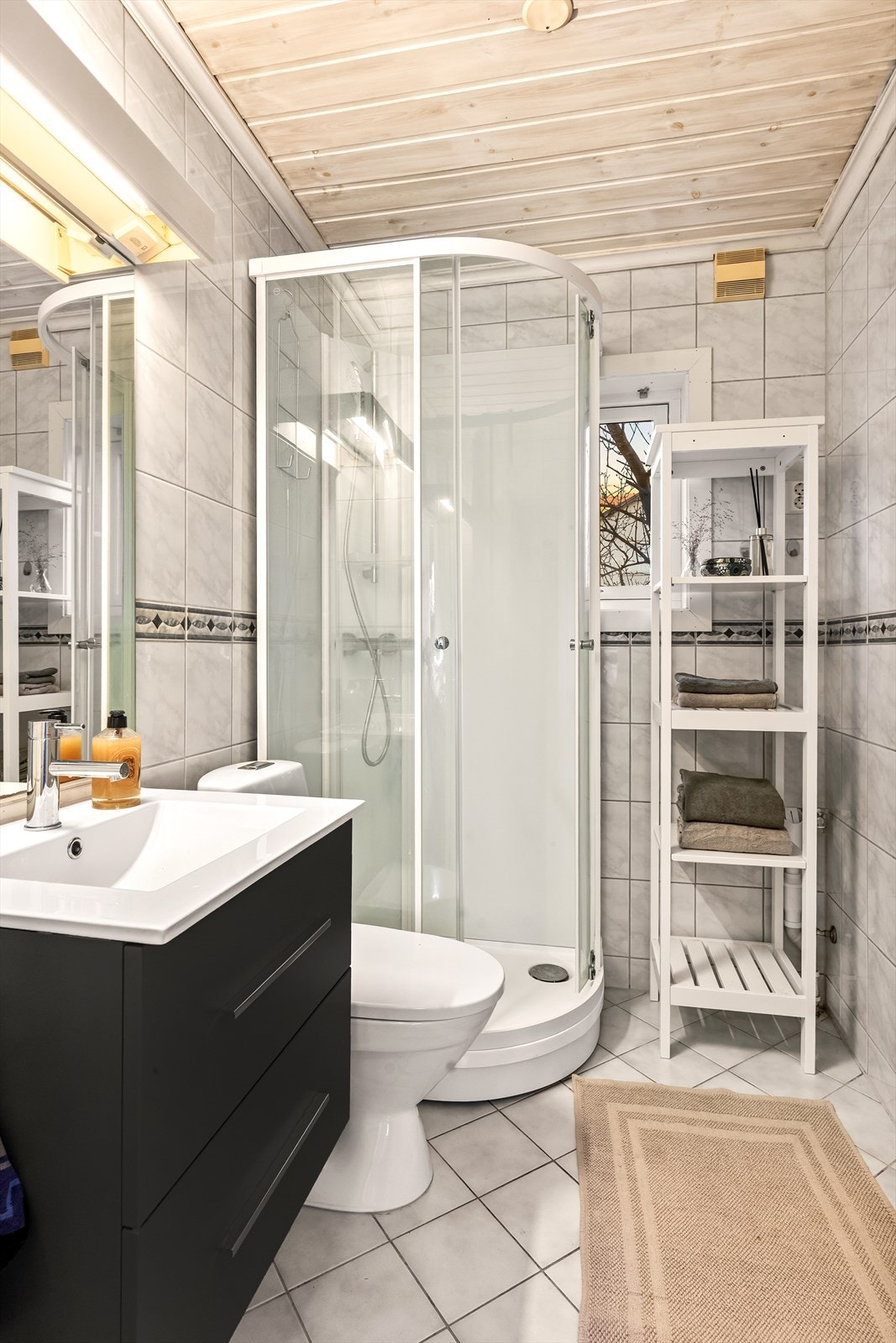 Flislagt bad utstyrt med dusjkabinett, servant med underskap og toalett. Praktisk planløsning og gode oppbevaringsmuligheter. Galleribilde