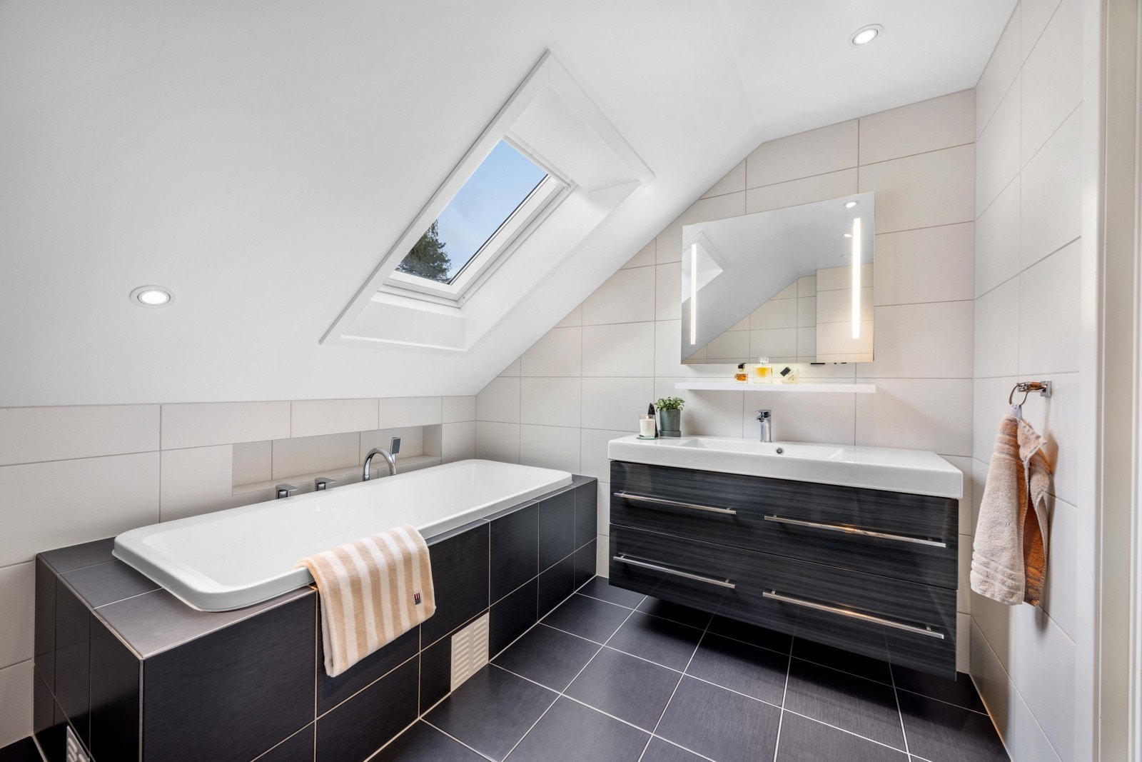 Badet har innmurt badekar, vegghengt toalett, servant i romslig innredning, veggskap og speil med innfelt lys Galleribilde