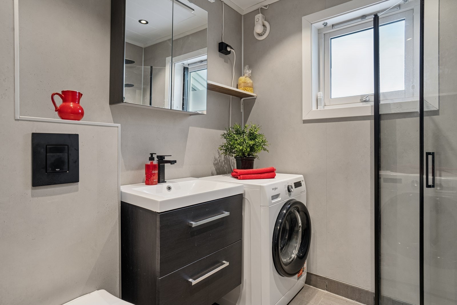 Badet er utstyrt med dusjhjørne, vegghengt wc, opplegg for vaskemaskin og en moderne baderomsinnredning. Galleribilde