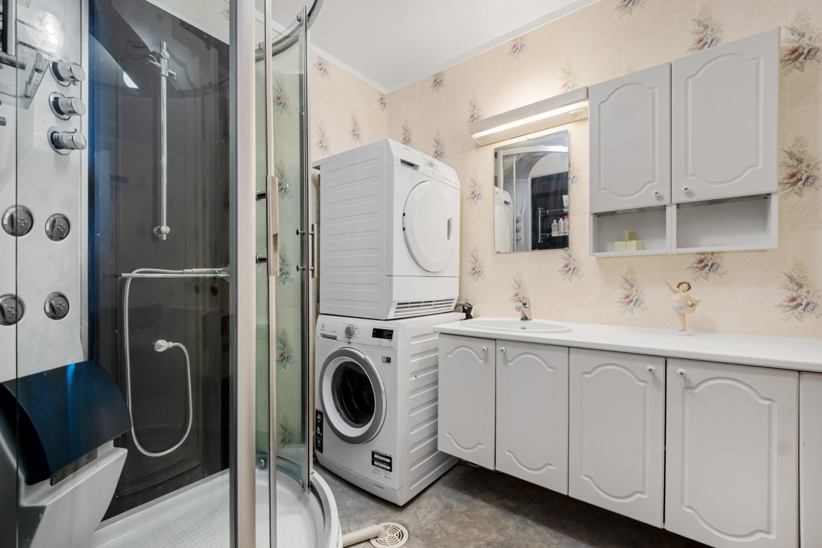 Badet har belegg på gulv, tapet på vegg, dusjkabinett, romslig innredning, og opplegg for vaskemaskin. Galleribilde