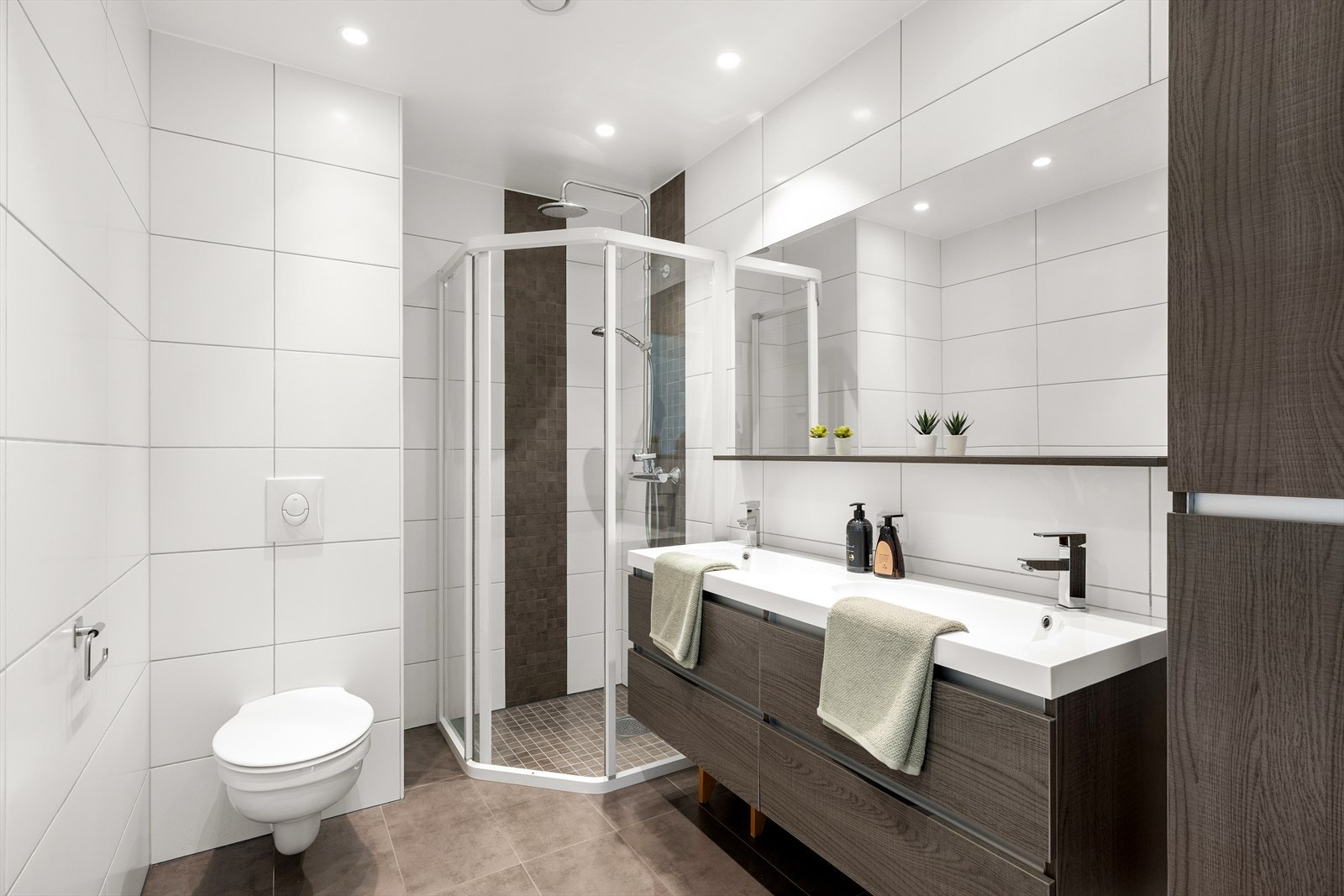 Pent, flislagt baderom innredet med seksjon med lagring i skuffer, dusjhjørne og vegghengt toalett. Galleribilde