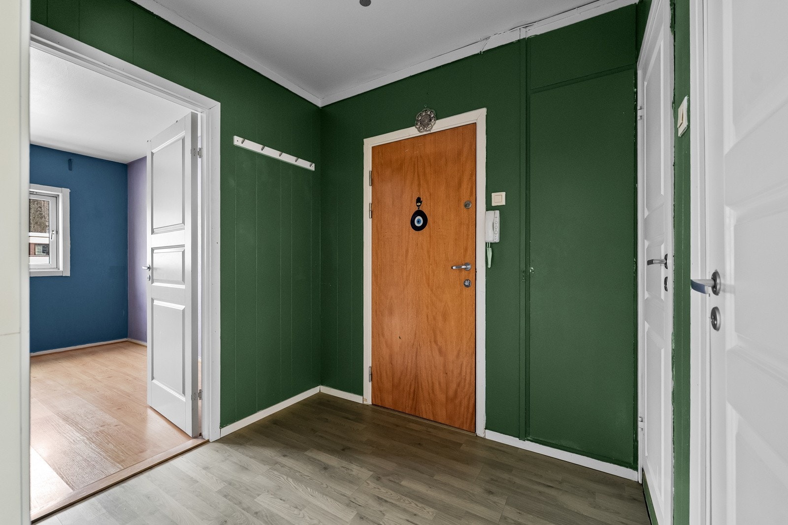 Entréen har malte veggflater og laminat på gulvet, og dørcalling er montert ved inngangsdøren. Galleribilde