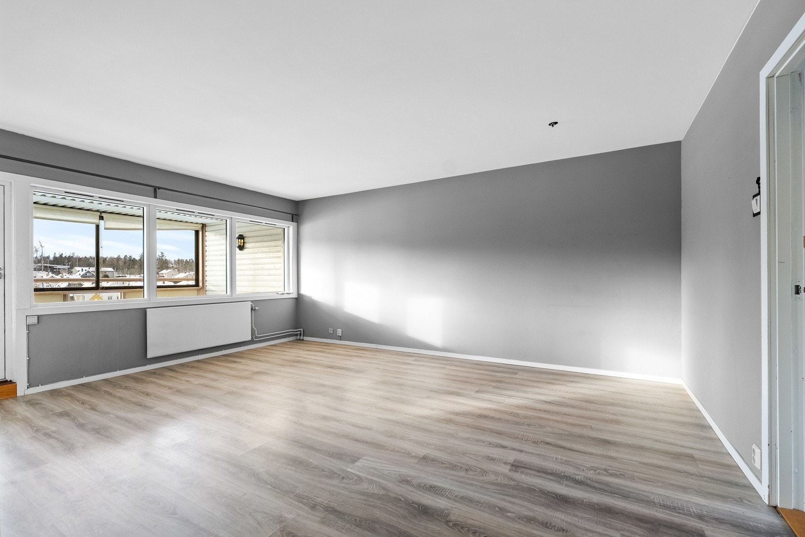 Den åpne stuen har malte veggflater og laminat på gulv. Store vindusflater slipper inn rikelig med lys og gir en luftig romfølelse. Galleribilde