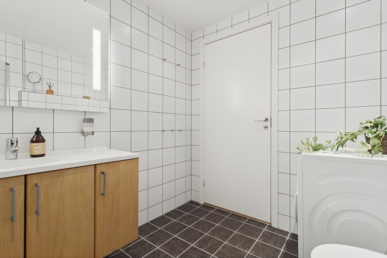 Badet er utstyrt med vegghengt toalett og baderomsinnredning med servant og god oppbevaringsplass. Dusjsonen er avgrenset med glassvegger og har dusjgarnityr montert på vegg. Opplegg for vaskemaskin. Galleribilde