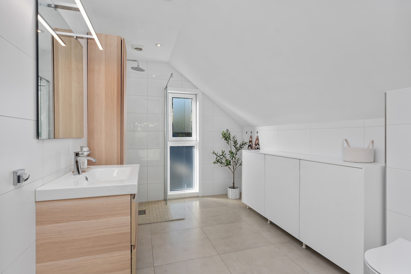 Tilbygget har et flott og tidløst bad med flislagt gulv og elektriske varmekabler. Her er dusjhjørne, veggjengt toalett og innredning med nedfelt servant. Galleribilde