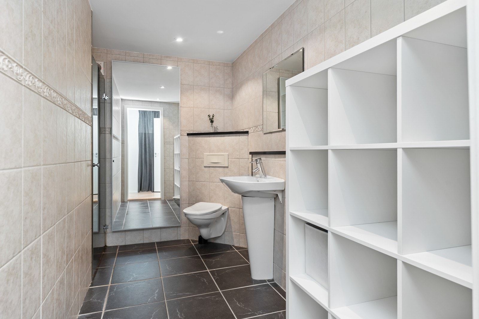 Bad har flislagt gulv og vegger hvor det er elektriske varmekabler i gulv. Rommet har dusjhjørne, vegghengt toalett og søylevask. Galleribilde