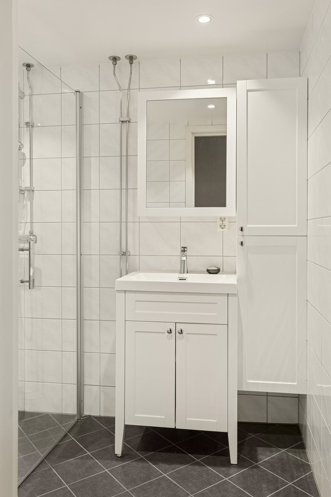 Baderommet har lys og innbydende innredning med mørke fliser i gulv. Varme i gulv Galleribilde